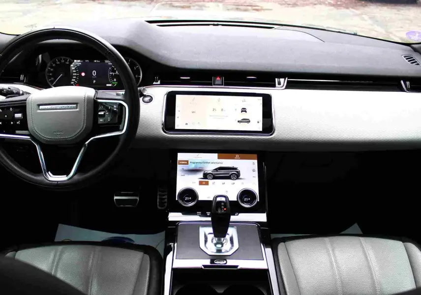 Intérieur du Range Rover Evoque 2023, vue de face sur le tableau de bord clair avec écran tactile et volant noir.