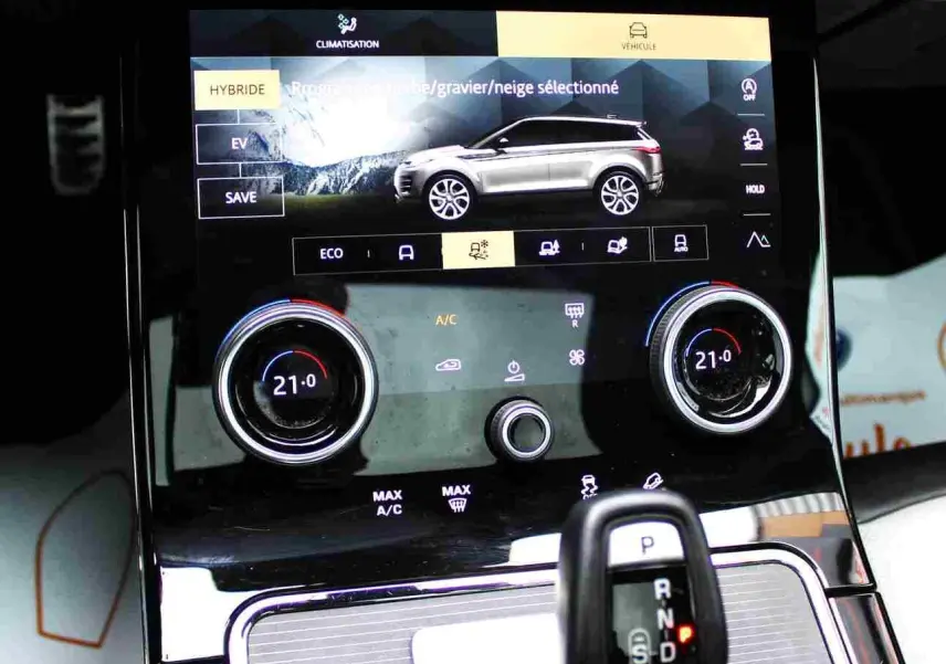 Vue rapprochée de la console centrale du Range Rover Evoque 2023 gris métal, affichant le mode hybride et la climatisation.