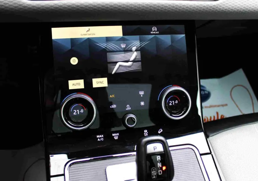 Gros plan sur la console centrale du Range Rover Evoque 2023 gris métal, affichant la climatisation digitale et le levier de vitesse.