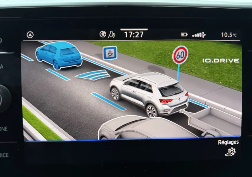 Affichage intérieur du système IQ.DRIVE montrant un Volkswagen T-Roc blanc 3/4 arrière avec remorque et signalisation 60 km/h.