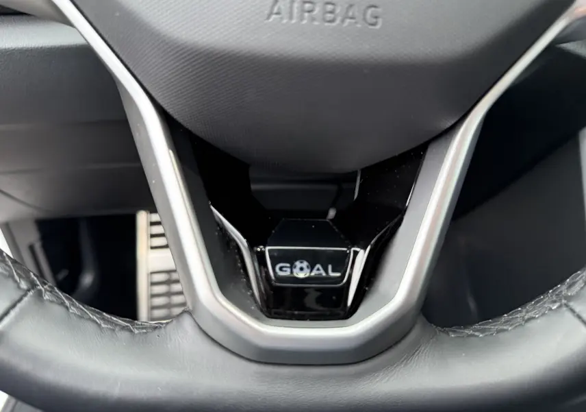 Gros plan sur le volant noir du Volkswagen T-Roc 2025 avec logo "GOAL" et inscription "AIRBAG" visible.