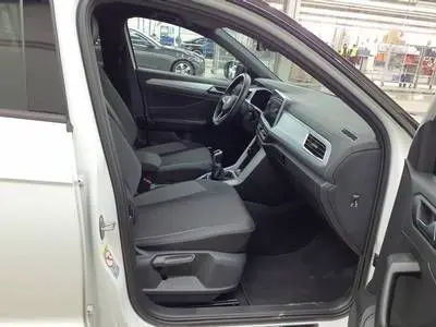 Vue intérieure côté conducteur du Volkswagen T-Roc blanc toit noir, montrant sièges et tableau de bord modernes.
