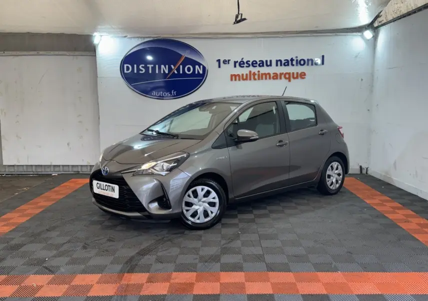 Toyota Yaris gris foncé vue 3/4 avant droit dans un showroom avec sol à damier noir et orange.