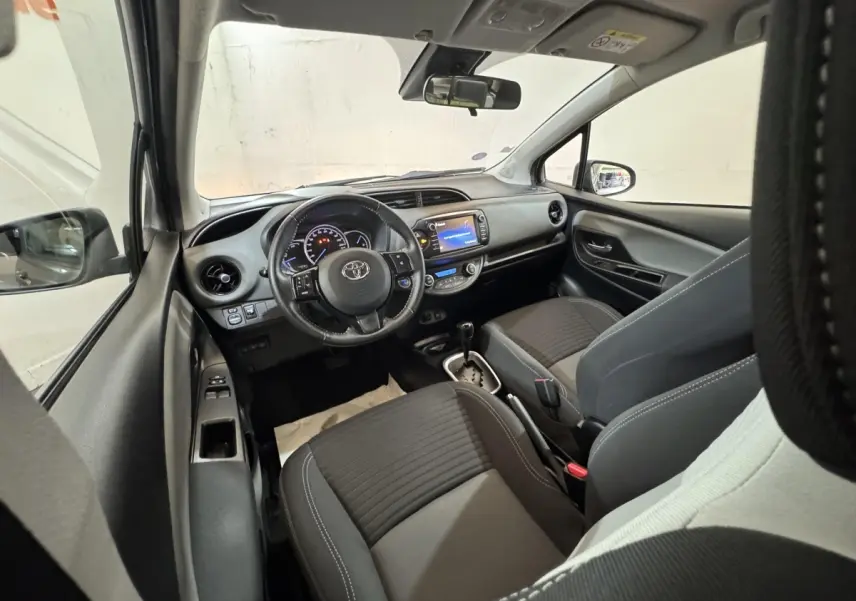 Vue intérieure avant de la Toyota Yaris 1.5 Hybrid 2019, montrant tableau de bord et sièges noirs avec volant multifonctions.