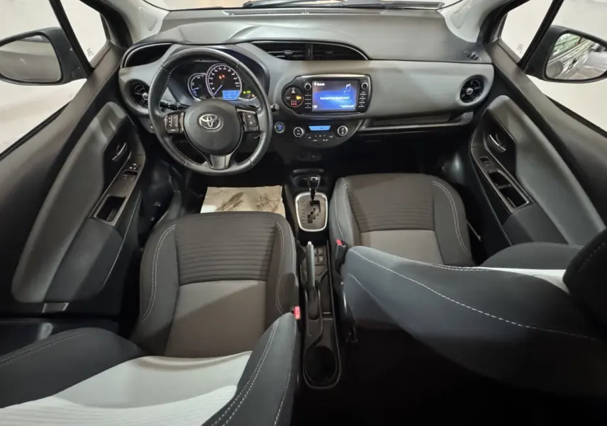 Vue intérieure avant de la Toyota Yaris 1.5 VVT-I Hybrid 2019, tableau de bord et sièges en tissu gris.