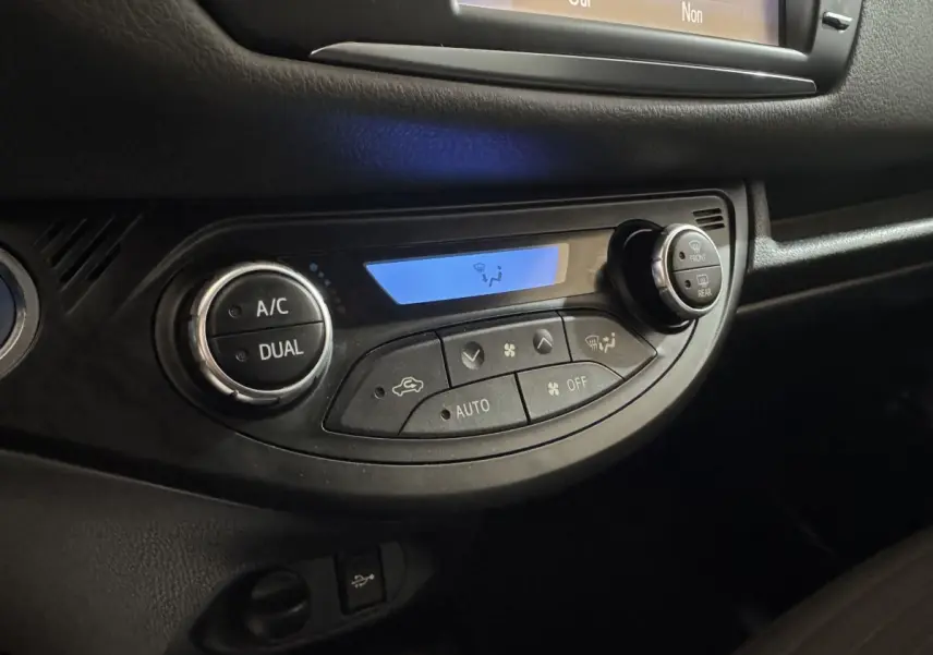 Gros plan sur la commande de climatisation digitale avec affichage bleu dans l'habitacle noir d'une Toyota Yaris gris foncé.