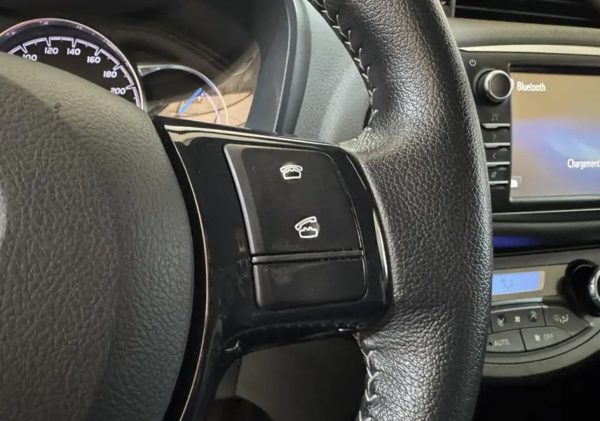 Gros plan sur le volant cuir noir de la Toyota Yaris hybride 2019, avec commandes téléphoniques et écran tactile Bluetooth visible.