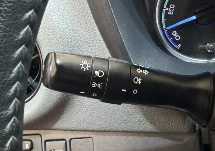 Gros plan sur la manette de commande des phares à gauche du volant dans l’habitacle gris d’une Toyota Yaris hybride 2019.