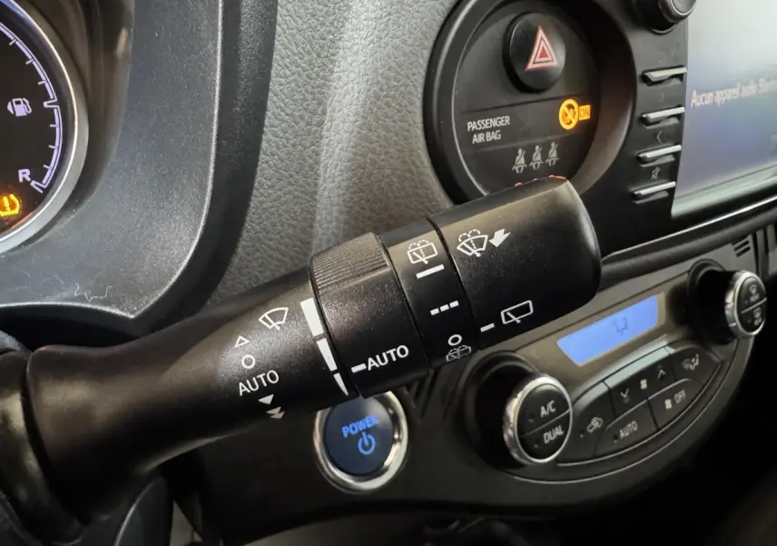 Gros plan sur la commande d’essuie-glace et le bouton démarrage bleu dans l’habitacle d’une Toyota Yaris gris foncé.