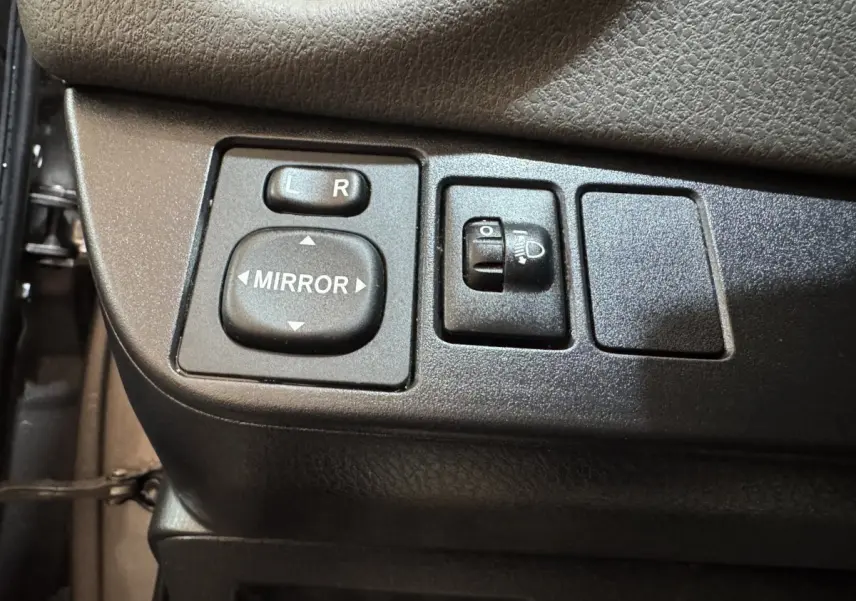 Gros plan sur les commandes de réglage des rétroviseurs et des phares sur la porte côté conducteur d'une Toyota Yaris gris foncé.