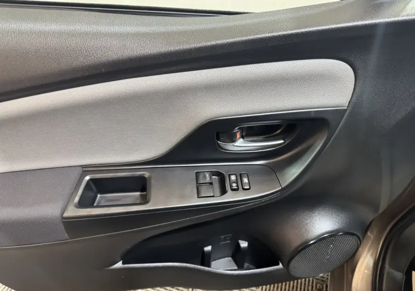 Vue intérieure côté conducteur de la porte d'une Toyota Yaris gris foncé, avec commandes de vitres et poignée noire.