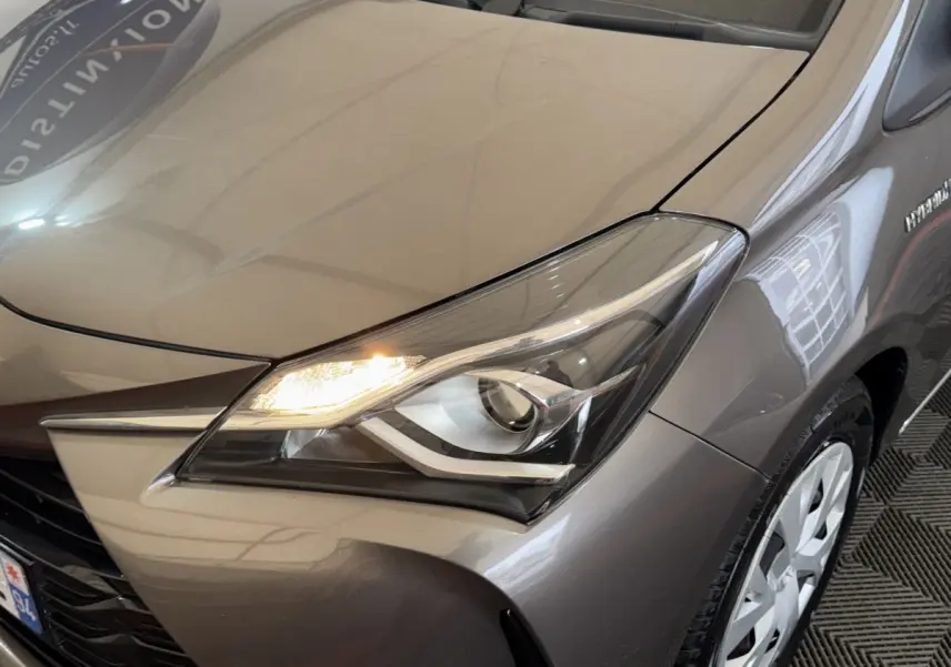 Gros plan sur l'avant droit gris foncé d'une Toyota Yaris 1.5 VVT-I Hybrid 2019 avec phare allumé et jante visible.