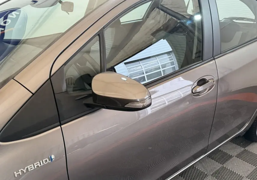 Vue latérale gauche rapprochée d’une Toyota Yaris hybride gris foncé avec rétroviseur et badge Hybrid visibles.