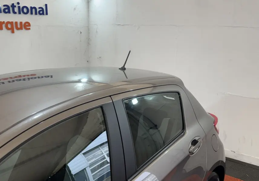 Vue latérale arrière droite d'une Toyota Yaris 1.5 VVT-I Hybrid gris foncé en intérieur, avec antenne de toit visible.
