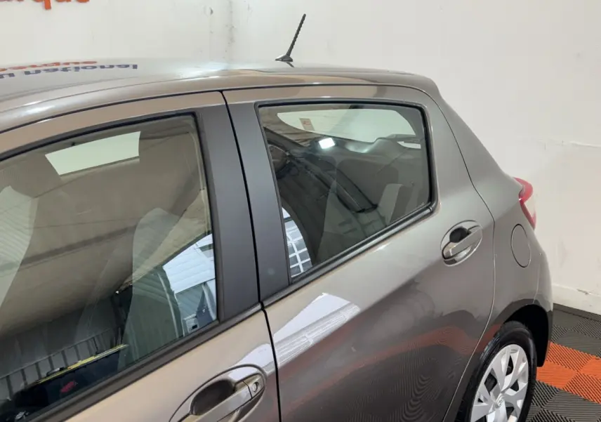 Vue latérale droite sur l'arrière d'une Toyota Yaris gris foncé avec poignée de porte et jante visible.