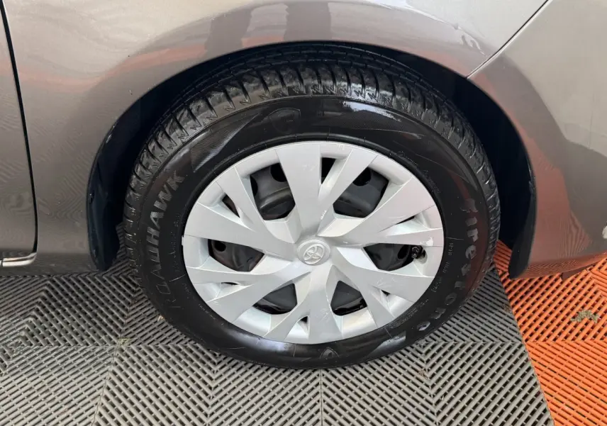 Gros plan sur la roue avant droite d’une Toyota Yaris gris foncé, mettant en valeur la jante en plastique et le pneu Firestone.
