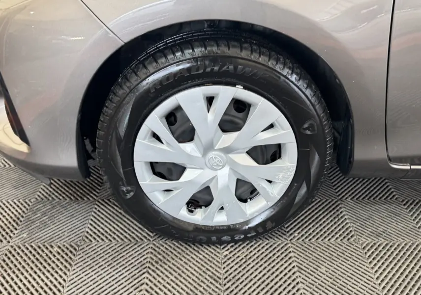 Gros plan sur la roue avant droite d'une Toyota Yaris gris foncé, avec enjoliveur argenté et pneu Firestone.
