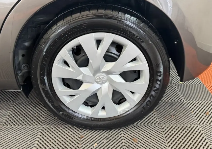 Gros plan sur la roue avant droite d'une Toyota Yaris gris foncé, avec enjoliveur argenté et pneu Dunlop.