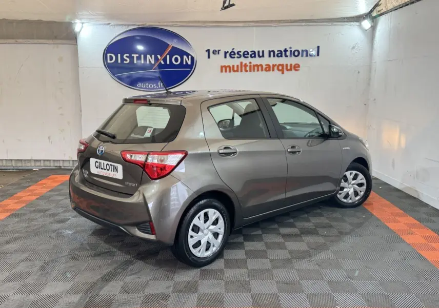 Toyota Yaris 1.5 VVT-I Hybrid gris foncé vue 3/4 arrière droit dans un showroom intérieur.