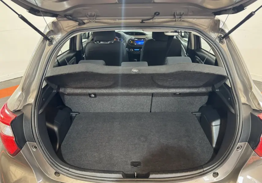 Vue arrière ouverte de la Toyota Yaris 1.5 VVT-I Hybrid gris foncé, montrant le coffre et l'intérieur avec tableau de bord éclairé.
