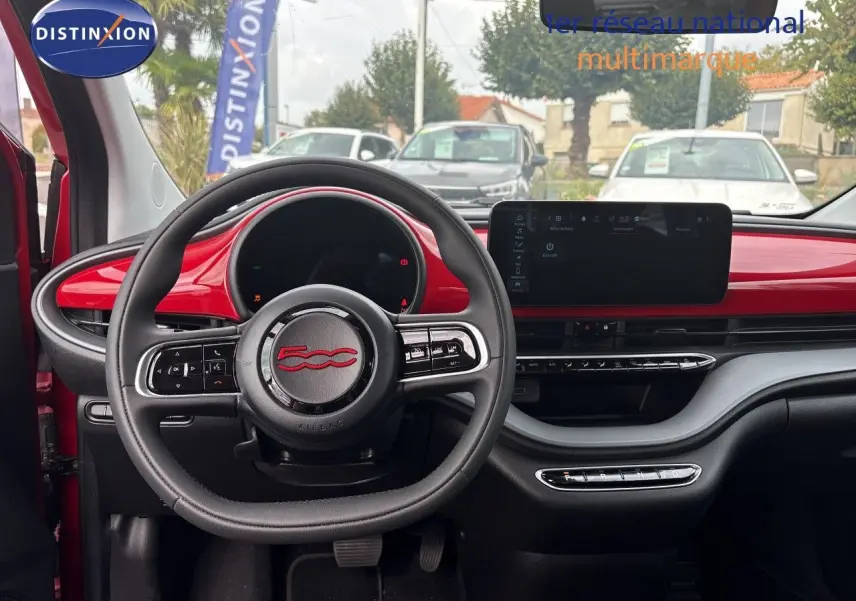 Intérieur de la FIAT 500e 2024 vue de face, tableau de bord rouge vif avec volant multifonction et écran tactile large.