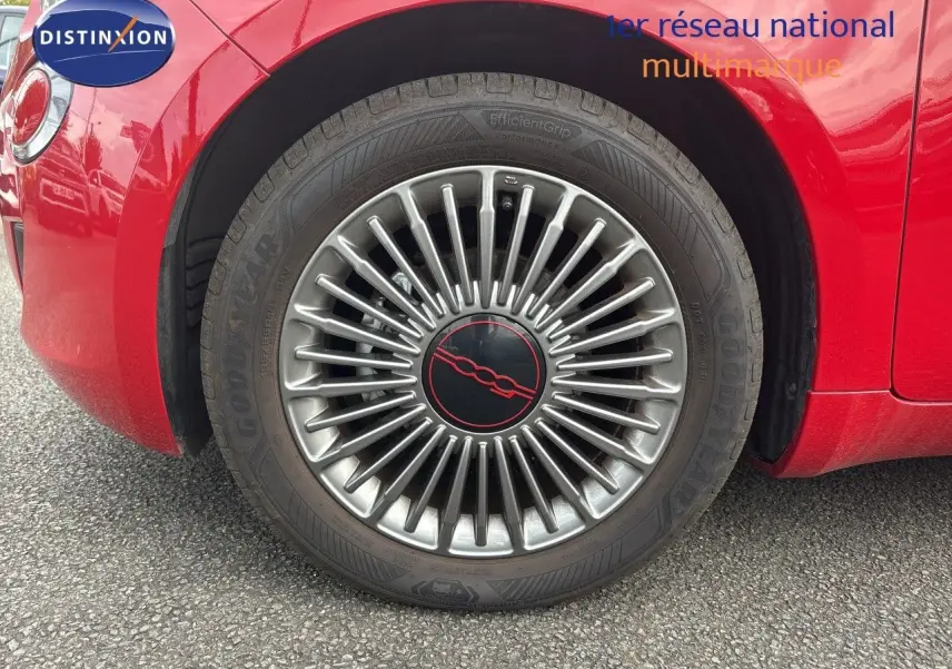 Gros plan sur la roue avant gauche d'une FIAT 500e rouge 2024 avec jante classique 15 pouces et logo central rouge.