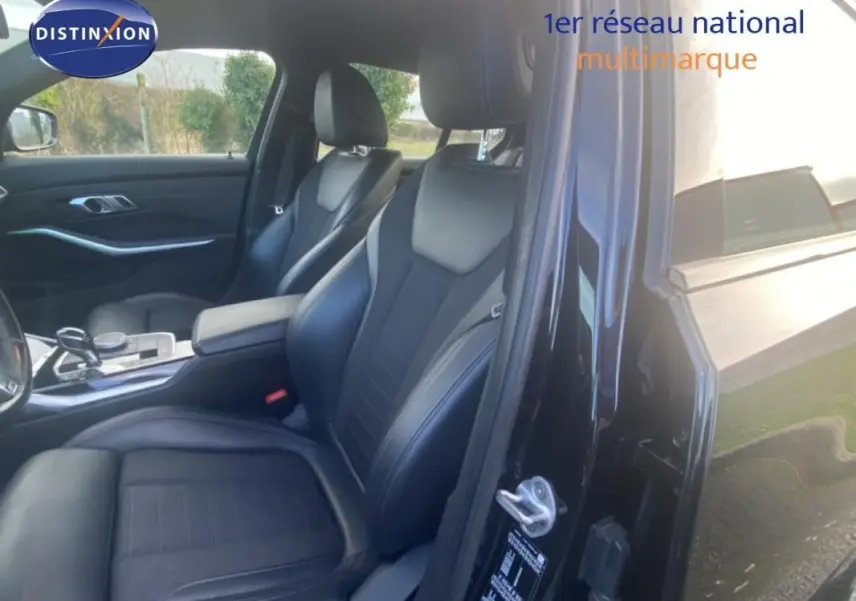 Vue intérieure côté conducteur de la BMW Série 3 G20 noire, mettant en valeur les sièges sport en cuir et l'accoudoir central.