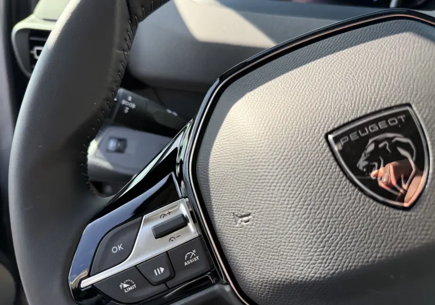 Gros plan sur le volant noir texturé du Peugeot Rifter Allure 2026, avec commandes intégrées et logo lion brillant.