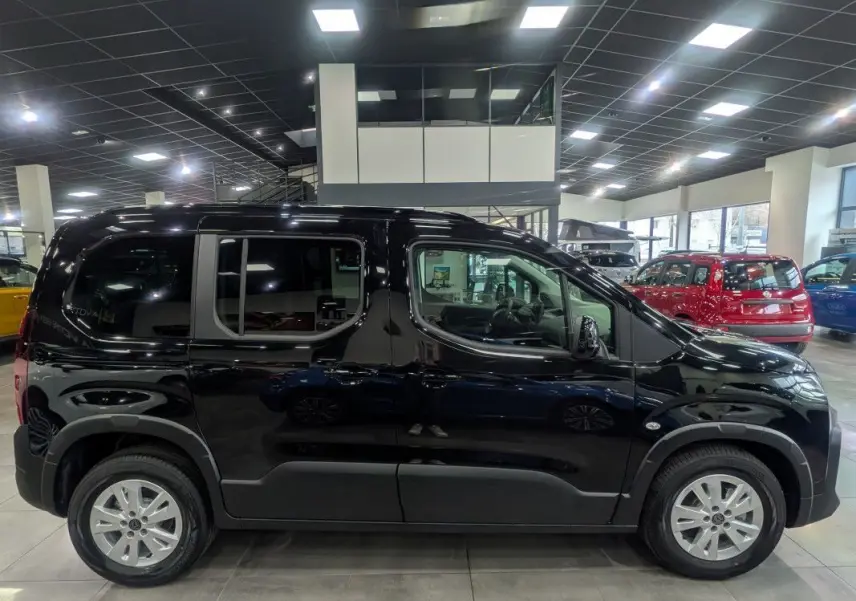 Vue de profil côté gauche d’un Peugeot Rifter Allure 2026 noir Perla Nera dans un showroom lumineux.