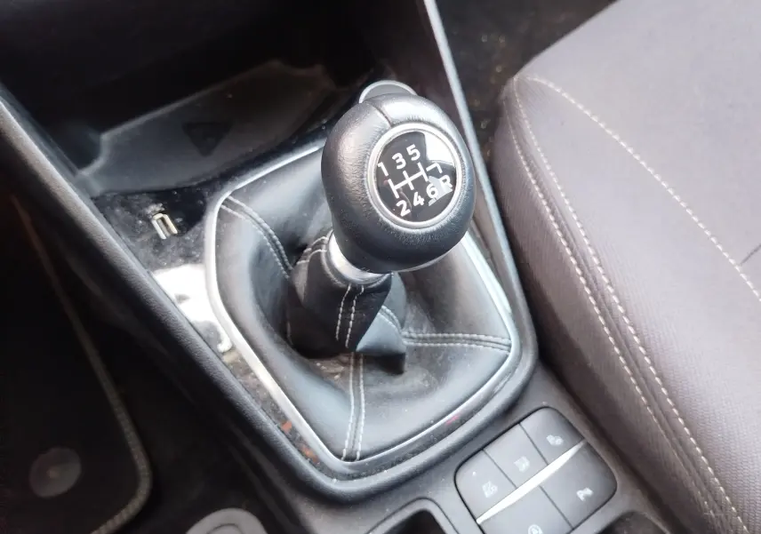 Vue rapprochée du levier de vitesses manuel noir avec coutures blanches dans une Ford Fiesta gris lunaire, console et siège partiellement visibles.