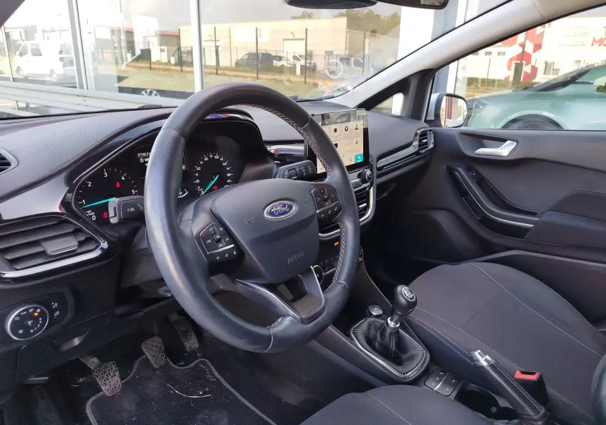 Vue intérieure côté conducteur de la Ford Fiesta gris lunaire, avec volant multifonction et boîte manuelle visible.