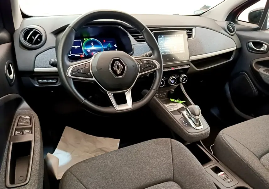 Vue intérieure avant de la Renault ZOE gris clair, montrant le volant, tableau de bord digital et écran tactile central.