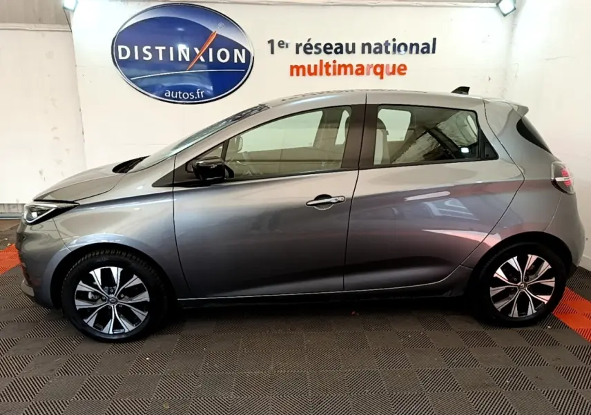 Vue de profil côté gauche d'une Renault ZOE gris clair Evolution R110 2022 en intérieur avec jantes noires et argentées.