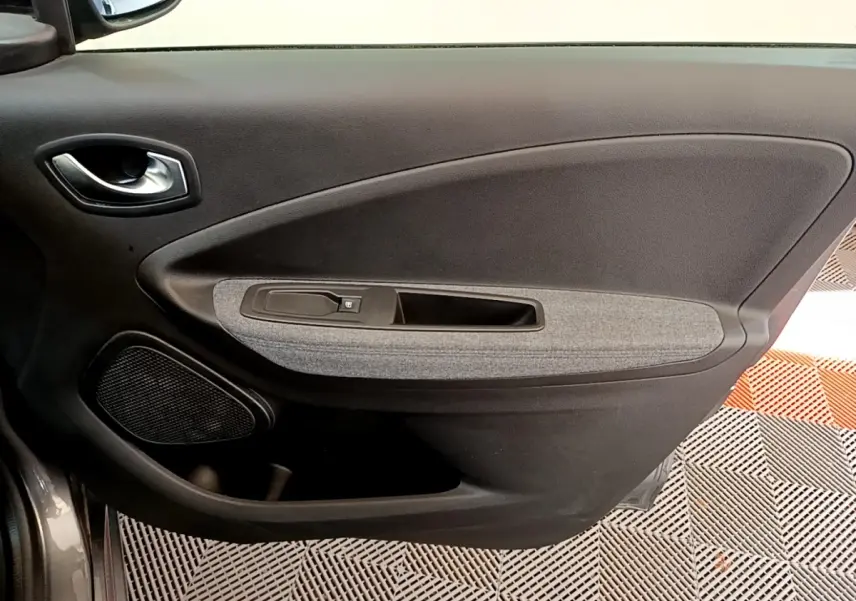 Vue rapprochée de la porte intérieure côté conducteur de la Renault ZOE gris clair, avec panneau tissu gris et commande de fenêtre.