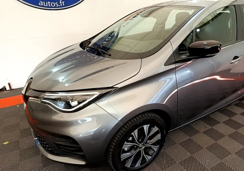 Vue 3/4 avant droit d'une Renault ZOE gris clair avec jantes noires et phares LED distinctifs.