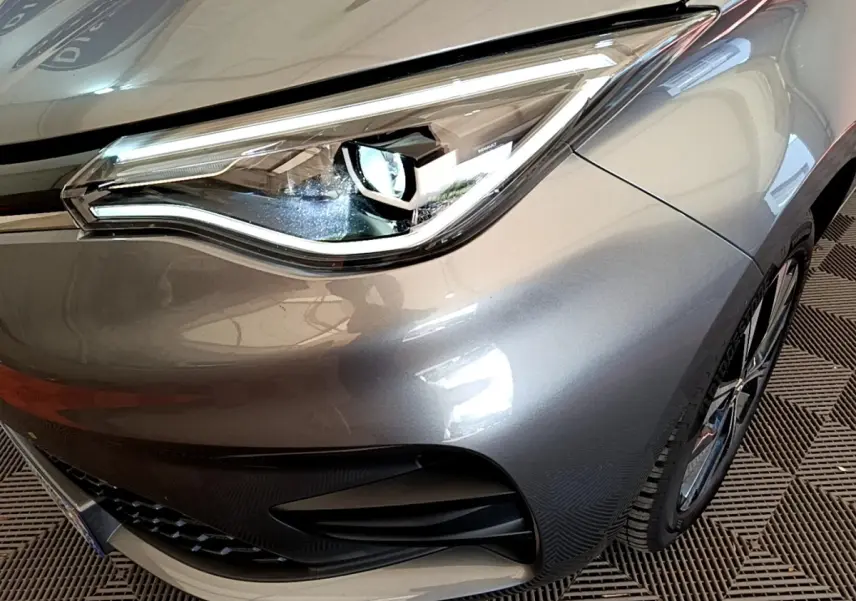 Gros plan sur le phare avant droit de la Renault ZOE gris clair, mettant en valeur le design LED et la calandre.