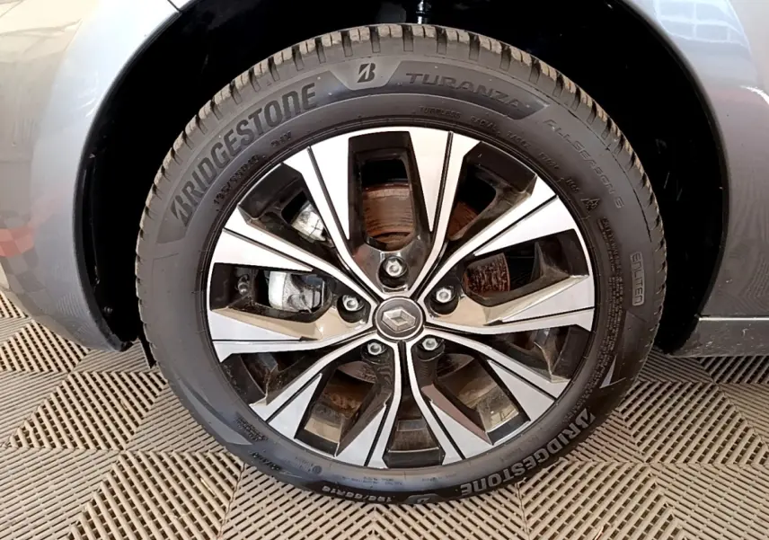 Gros plan sur la roue avant droite d’une Renault ZOE gris clair, jante alliage à design moderne avec logo Renault central.