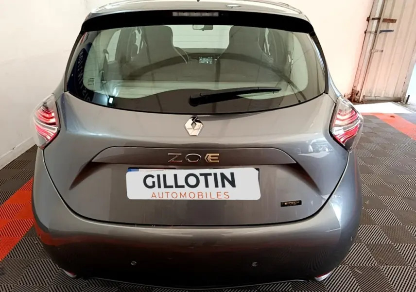 Vue arrière d'une Renault ZOE gris clair avec feux LED et logo ZOE E-Tech visible sur un sol à damier noir et rouge.