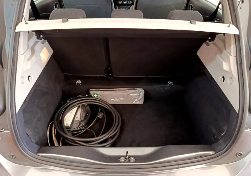 Coffre ouvert d’une Renault ZOE gris clair vue arrière, avec câble de charge et trousse de sécurité visibles.