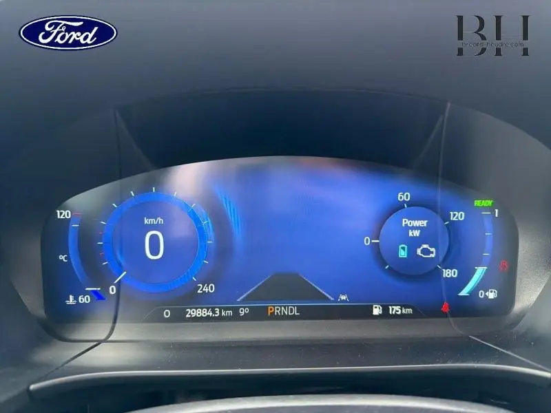 Tableau de bord numérique bleu du Ford Kuga 2023, affichant vitesse, puissance et autonomie, vue frontale rapprochée.