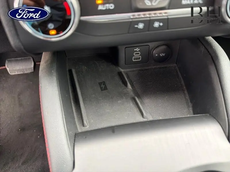 Gros plan sur la console centrale noire du Ford Kuga 2023 avec ports USB, prise 12V et zone de charge sans fil.