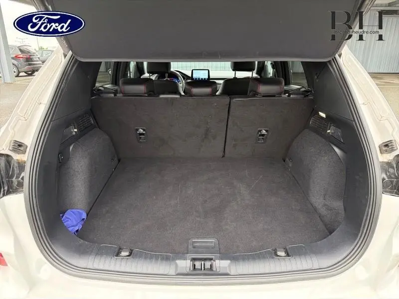 Vue arrière du coffre ouvert du Ford Kuga blanc Premium Platinum 2023, montrant l'espace de chargement et la banquette arrière noire.