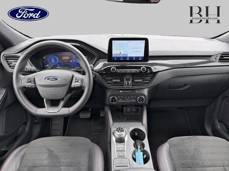 Vue intérieure avant du Ford Kuga 2023 avec tableau de bord moderne, écran tactile central et volant cuir multifonction.
