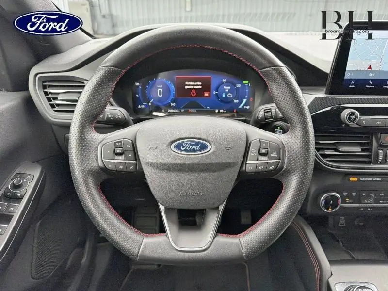 Vue intérieure centrée sur le volant cuir noir à surpiqûres rouges du Ford Kuga 2023 avec tableau de bord numérique et écran tactile.