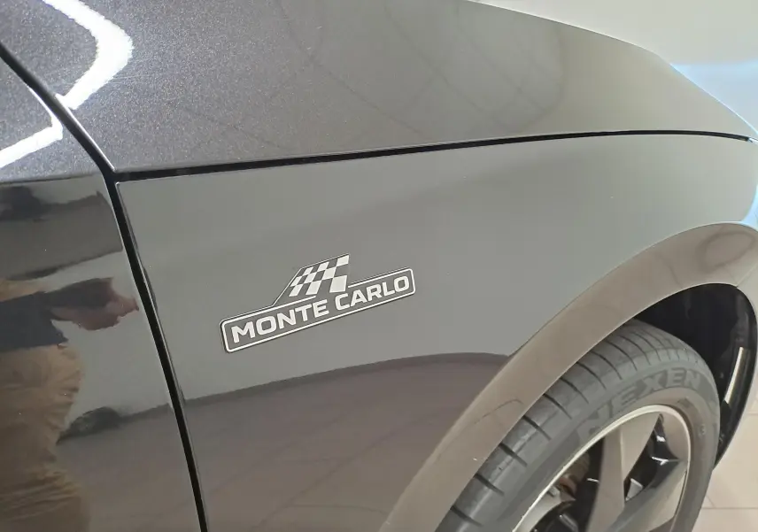 Gros plan sur l'aile avant gauche noire nacrée d'une Skoda Scala Monte-Carlo avec logo distinctif et jante noire.