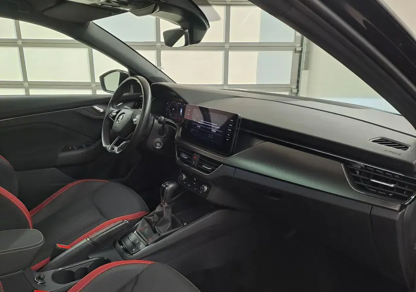 Intérieur de la Skoda Scala 2022 vu côté conducteur, sièges noirs avec surpiqûres rouges et tableau de bord moderne.