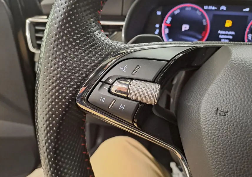 Gros plan sur la commande audio à gauche du volant perforé avec surpiqûres rouges d'une Skoda Scala noire 2022.