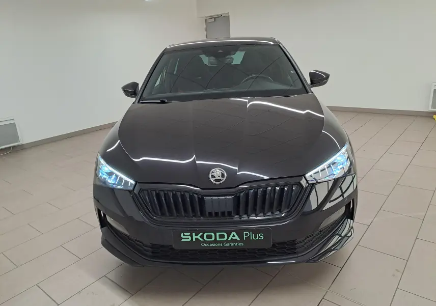Vue de face d'une Skoda Scala 1.0 TSI Monte-Carlo noire nacrée avec phares allumés dans un showroom lumineux.