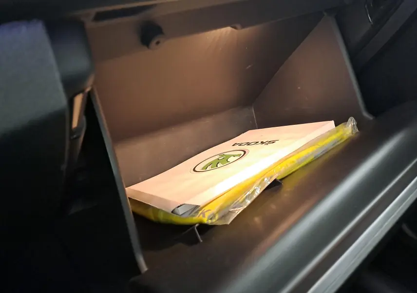 Vue rapprochée de la boîte à gants ouverte d'une Skoda Scala noire avec manuel et gilet jaune à l'intérieur.
