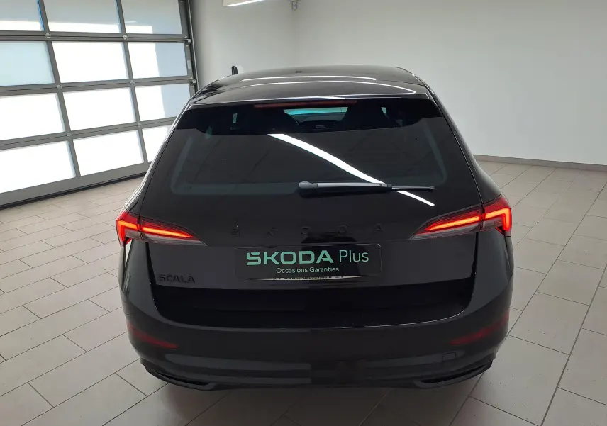 Vue arrière d'une Skoda Scala 2022 en Noir Magic nacré avec feux arrière allumés dans un garage lumineux.